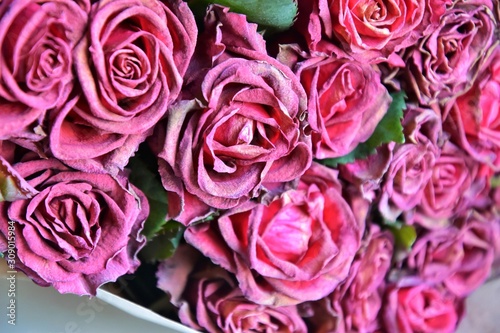 Fading bouquet of red roses in craft paper with selective focus and blurred petals on front. Wilted bunch of flower on blurred background. Dying romantic bouquet of flowers. Dried flowers 