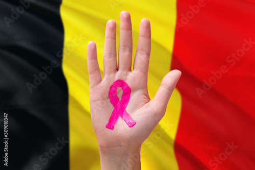 Belgium awareness concept. Close-up awareness ribbon painted on palm on national flag background. October Pink day and world cancer day.
