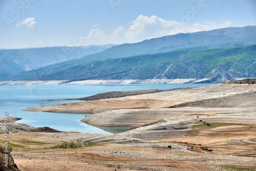 a sandy beach on a blue lake in the mountains