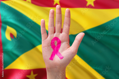 Grenada awareness concept. Close-up awareness ribbon painted on palm on national flag background. October Pink day and world cancer day.