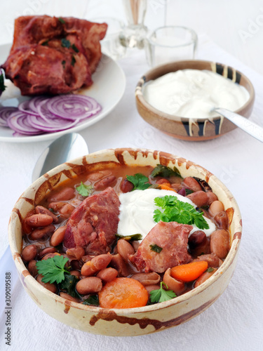 Photography Pinto bean soup with smoked ham hock in bowl with sour cream and red onions on t