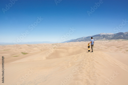 young man with sand board on sand dune in great sand dunes national park colorado