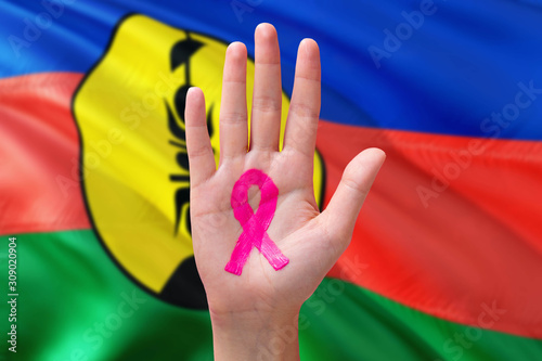 New Caledonia awareness concept. Close-up awareness ribbon painted on palm on national flag background. October Pink day and world cancer day.