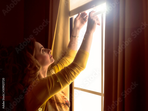 Home blinds window shades woman opening shade blind during sunny morning. Mature woman holding modern cordless top down luxury curtains indoors.