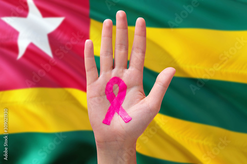 Togo awareness concept. Close-up awareness ribbon painted on palm on national flag background. October Pink day and world cancer day.