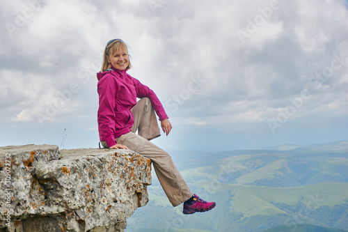 a smiling woman sitting on a cliff in the mountains