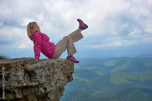 a smiling woman sitting on a cliff in the mountains
