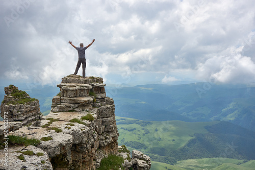 the man stands on a high cliff and stretches his arms