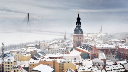 Panoramic aerial view of the Riga old town and Daugava river from St. Peter's Church in winter. Morning fog, snow-covered cable-stayed bridge, cathedral, houses. Latvia. Landmarks, sightseeing