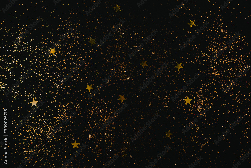 Golden sparkles and stars on black backdrop. Holiday concept.