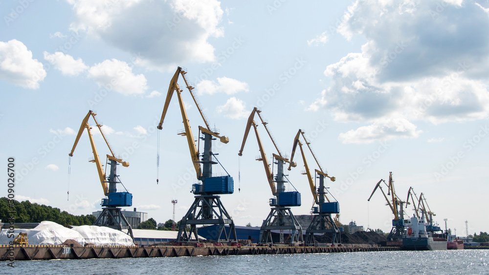 the group of cargo cranes on the shore on a background of sky and Cumulus clouds. the group of cargo cranes on the shore on a background of sky and Cumulus clouds.