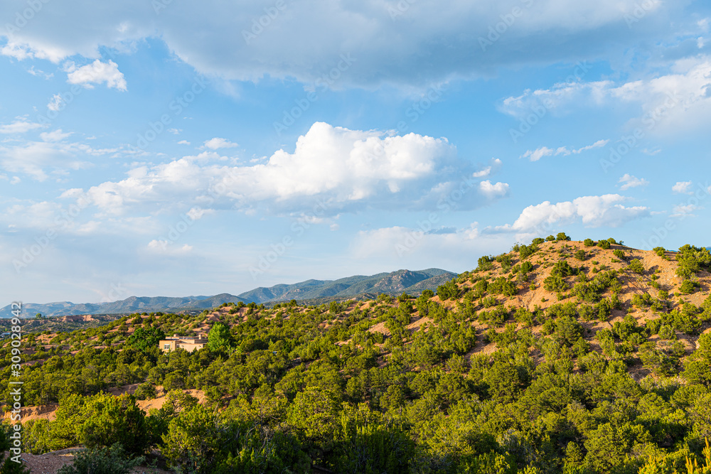 Fototapeta premium Zachód słońca w Santa Fe w górach Nowego Meksyku w sąsiedztwie społeczności Tesuque z domami zielone rośliny pignon drzewa krzewy i błękitne niebo chmury