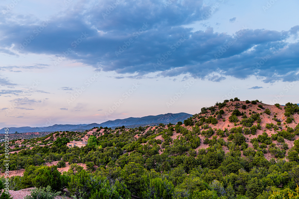 Sunset pink twilight in Santa Fe, New Mexico mountains Tesuque community neighborhood with houses green plants pignon trees shrubs and blue sky clouds