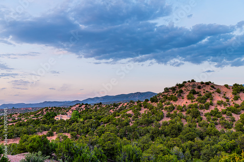 Sunset pink twilight in Santa Fe  New Mexico mountains Tesuque community neighborhood with houses green plants pignon trees shrubs and blue sky clouds