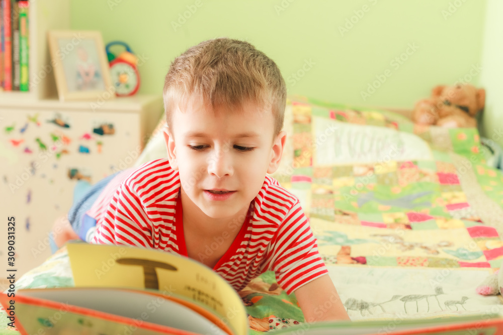 Happy boy reading alphabet book. Preschool kid laying on bed with smiling face and looking at open book. Home school education Happy boy reading alphabet book. Preschool kid laying on bed with smiling face and looking at open book. Home school education