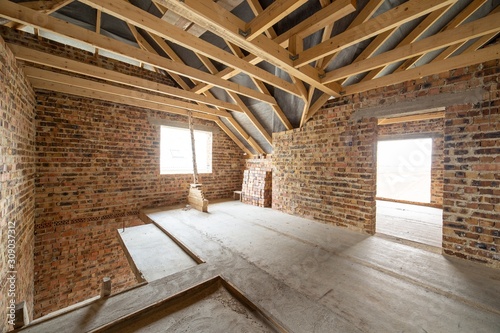 фотографія Interior of unfinished brick house with concrete floor, bare walls ready for plastering and wooden roofing frame attic under construction
