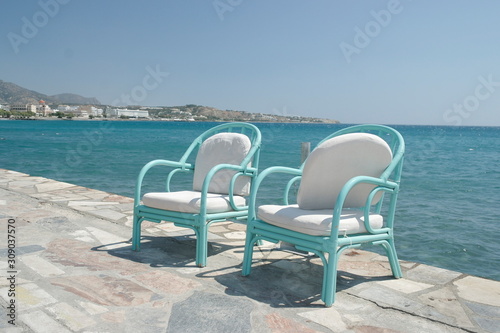 wooden turquoise chairs with soft cushions stand on the waterfront next to the blue sea