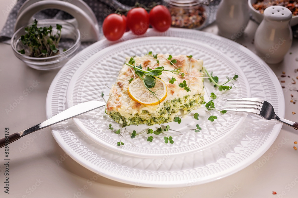 Close-up vegetarian lasagna with spinach and microgreens on a white plate. Tasty and healthy mediterranean food.