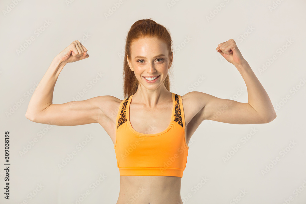 beautiful young woman with red hair in sportswear shows her muscles on a white background beautiful young woman with red hair in sportswear shows her muscles on a white background