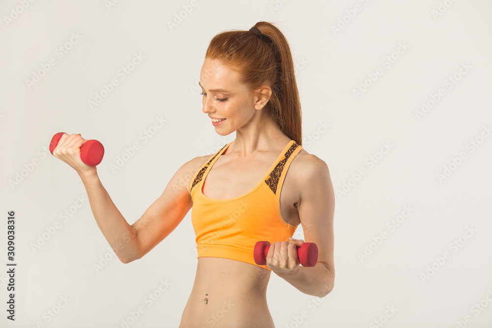 beautiful young woman with red hair with dumbbells in hands on a white background beautiful young woman with red hair with dumbbells in hands on a white background