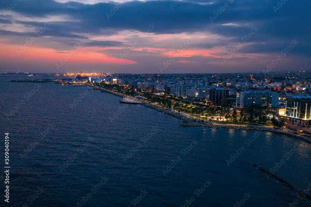 Aerial night panorama of Limassol, Cyprus waterfront. Famous mediterranean city resort in evening with Molos Park, promenade or embankment and buildings, from above view.
