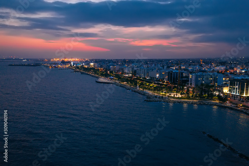Aerial night panorama of Limassol, Cyprus waterfront. Famous mediterranean city resort in evening with Molos Park, promenade or embankment and buildings, from above view.