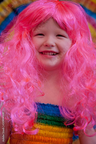 Happy Cute caucasian boy changed clothes at carnival in dress of girl of rainbow color. Pink doll wig. LGBT color background. Education in kindergarten and preschool children. hair coloring