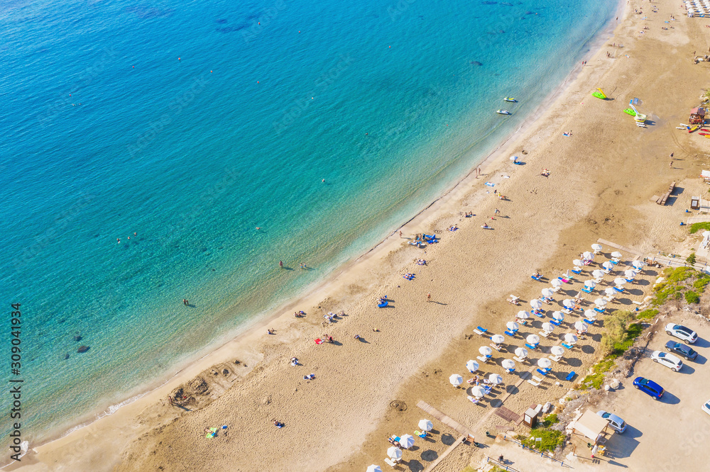 Aerial view of beautiful Coral beach in Paphos with azure seawater, Cyprus. Sand coast with umbrellas, sunbeds, people and clear sea water.