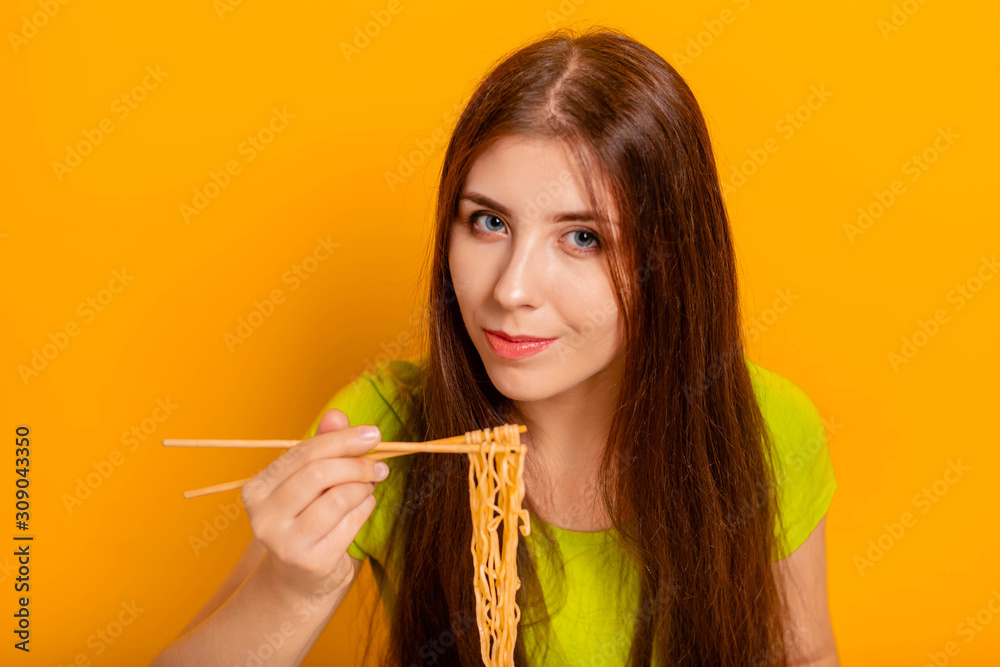 Woman eating instant noodles with chinese chopsticks. Studio photo on a yellow background. Woman eating instant noodles with chinese chopsticks. Studio photo on a yellow background.