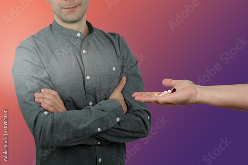 female hand holds out, offers a man with crossed arms a handful of colored pills and capsules, close-up, copy space, treatment concept