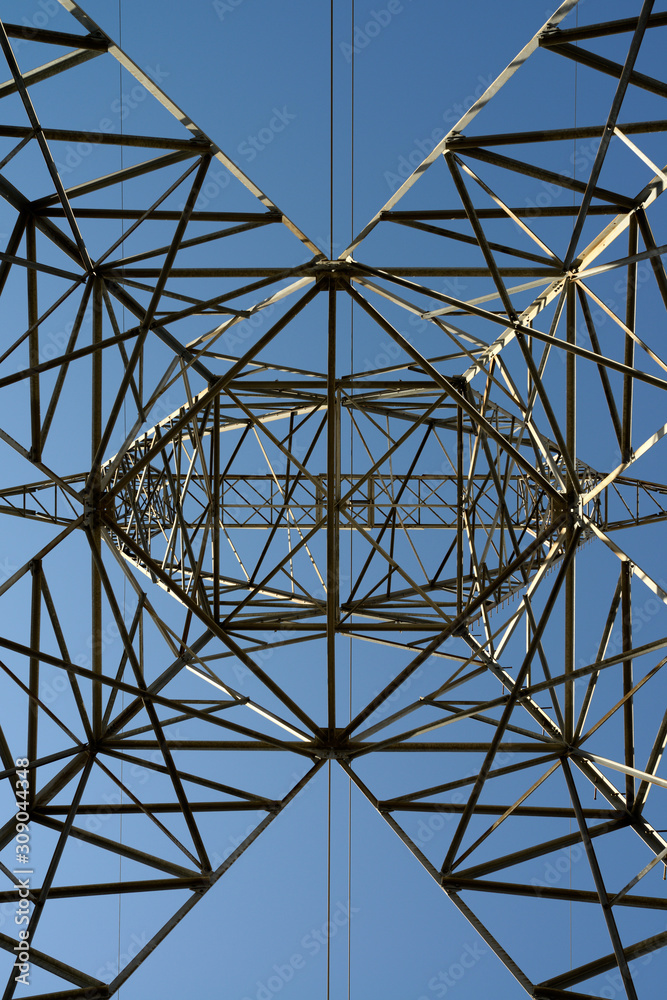 Abstract latticework looking up a steel suspension electric tower with high tension power lines and a blue sky