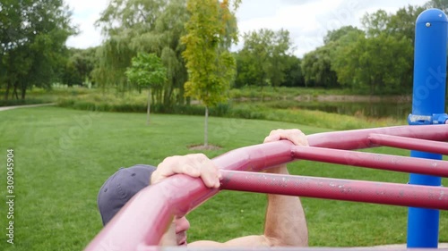 Man exercising, strength training, working out doing body weight underhand pull ups in the park.