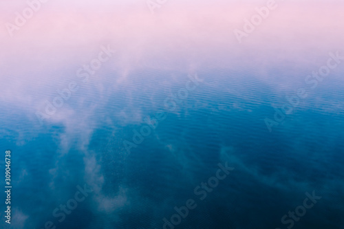Pink fog over blue water surface, aerial view. Tranquil natural background