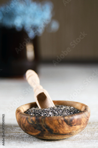 Edible seeds of chia, Salvia hispanica, a flowering plant of the mint family. Vertical orientation. Chia seeds in a plate of natural olive wood. Product for beauty and health. Proper nutrition.