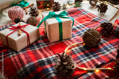 Christmas gifts on the background of a red woolen checkered plaid with garlands of cones and fir branches