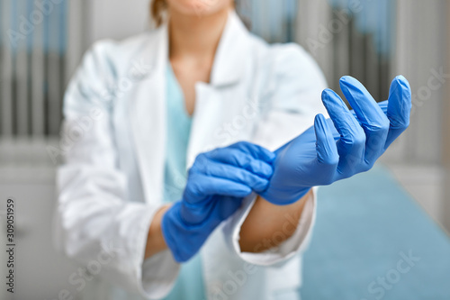 Close up of a female doctor putting a blue latex gloves on a clinic background. photo