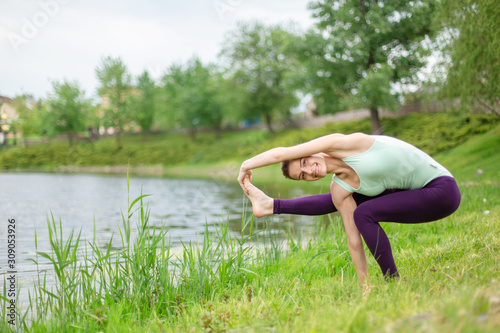 A young sports girl practices yoga on a green lawn by the river, yoga assans posture. Meditation and unity with nature photo