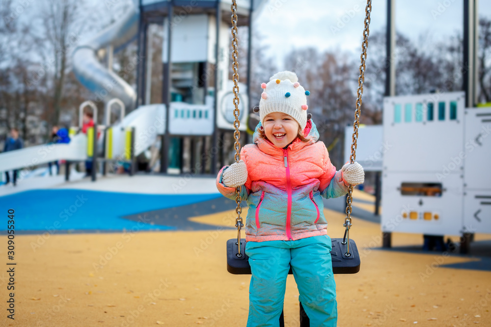 Adorable little girl on the playground. Toddler having fun on a swing on beautiful winter day