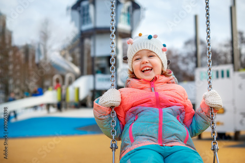 Adorable little girl on the playground. Toddler having fun on a swing on beautiful winter day