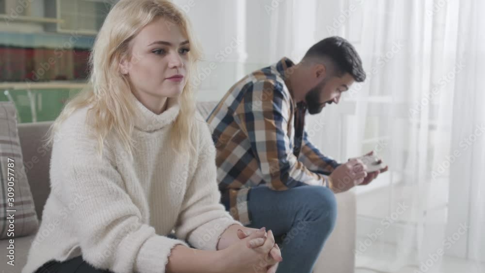 Young upset Caucasian girl looking away as bearded man sitting at the background. Husband and wife having difficulties in relationship. Breakup, misunderstanding, divorce. Young upset Caucasian girl looking away as bearded man sitting at the background. Husband and wife having difficulties in relationship. Breakup, misunderstanding, divorce.