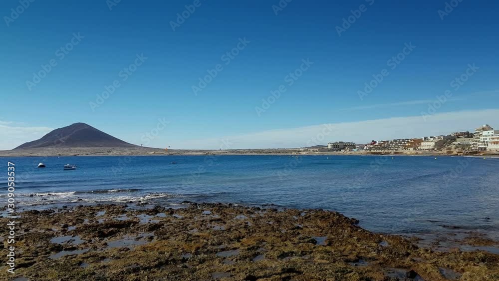 Kite surfing in El Medano, Tenerife, Canary Islands. 4K UHD footage of ocean bay, rocky beach and small silhouettes of kiters, boats. Panoramic view. Water sports activity concept