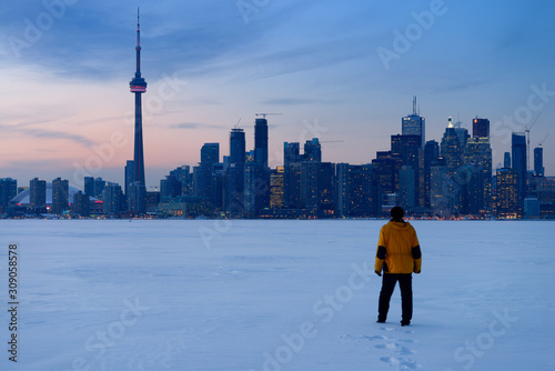 Man walking in fresh snow on frozen Lake Ontario with Toronto city skyline in winter
