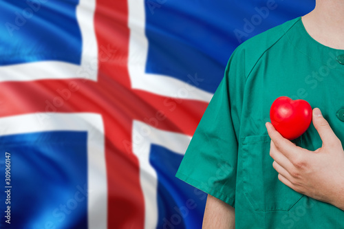 Iceland veterinary clinic concept. Veterinarian is holding plastic heart in green uniform on national flag background. Animial love theme. photo