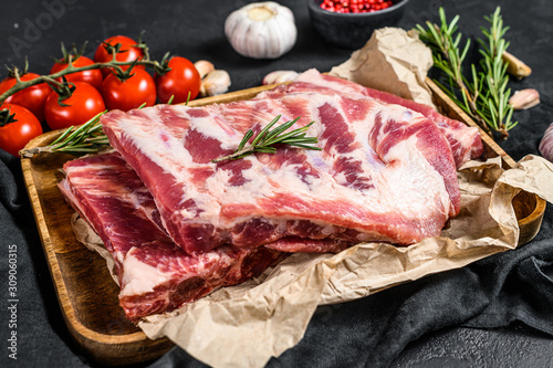 Fresh raw pork ribs with rosemary and garlic in a wooden bowl. Black background. Top view