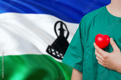 Lesotho veterinary clinic concept. Veterinarian is holding plastic heart in green uniform on national flag background. Animial love theme. photo