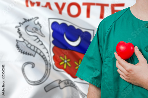 Mayotte veterinary clinic concept. Veterinarian is holding plastic heart in green uniform on national flag background. Animial love theme.