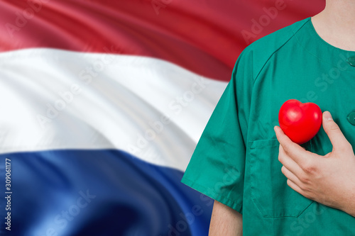 Netherlands veterinary clinic concept. Veterinarian is holding plastic heart in green uniform on national flag background. Animial love theme. photo