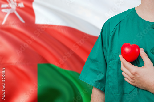 Oman veterinary clinic concept. Veterinarian is holding plastic heart in green uniform on national flag background. Animial love theme. photo