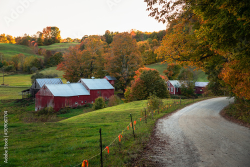 Traditional American red barn along a gravel road in a rolling autumnal landscape at sunset. Woodstock, VT, USA.