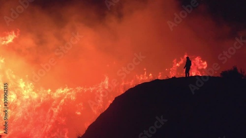 Slow motion shot, of a silhouette man standing on a hill, in front of burning nature of the Californian wildfires, at night time, in Northridge, Los Angeles, California, USA